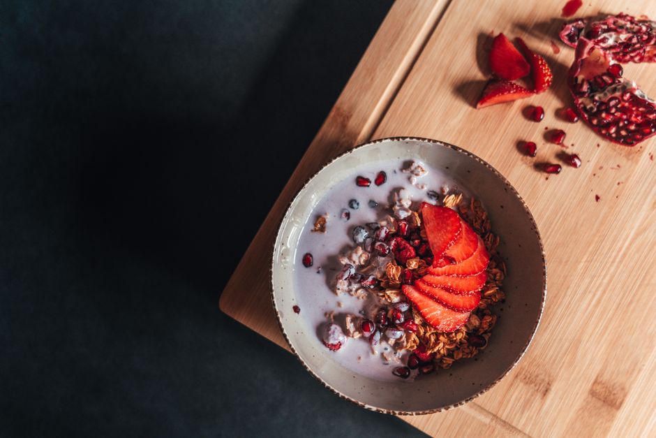 Granola bowl topped with fresh strawberries and pomegranate seeds on a wooden cutting board.