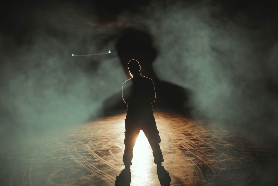 A dramatic silhouette of a man standing in smoke with backlighting, creating a mysterious atmosphere.