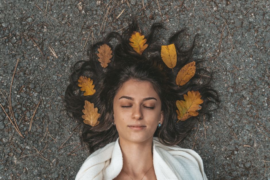 Peaceful woman with closed eyes surrounded by autumn leaves on a gravel path in İstanbul.