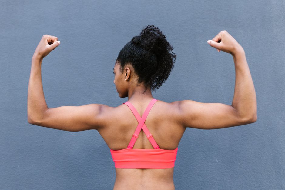 Rear view of a fit woman flexing muscles in a pink sports bra against a gray background.