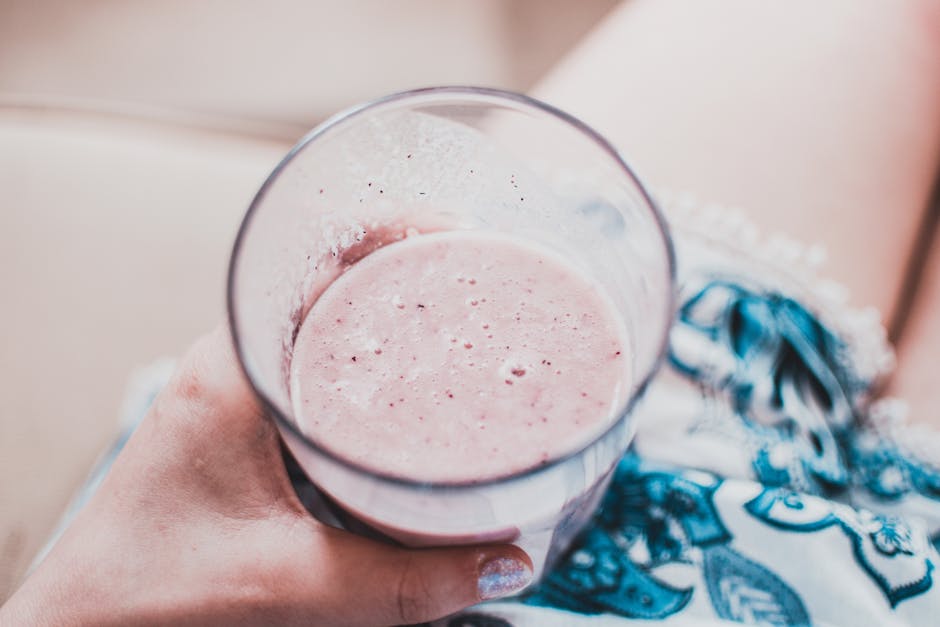 Close-up of a person holding a creamy strawberry smoothie in a glass, perfect for a refreshing treat.