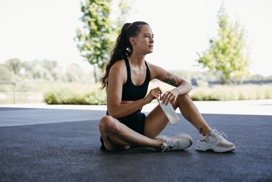 A young woman resting outdoors with a water bottle, taking a break after exercise.