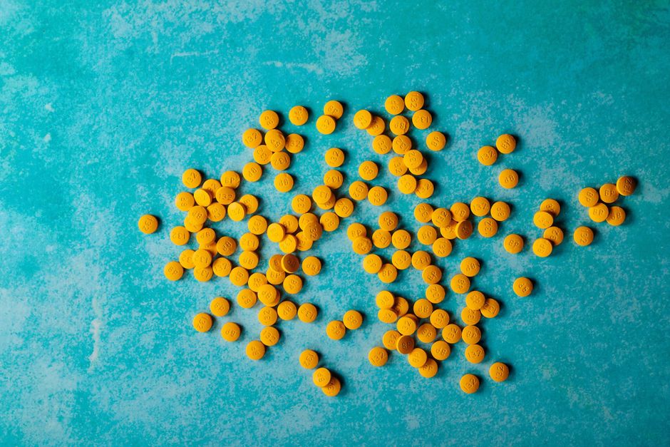 Close-up of scattered yellow pills on a vibrant turquoise background, top view.