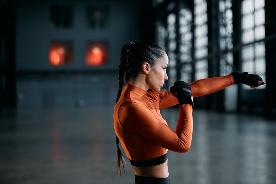 Side view of a woman in orange activewear practicing boxing indoors, exuding focus and determination.
