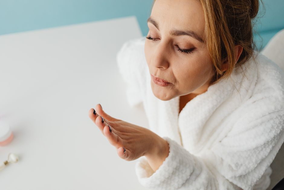 Woman in a bathrobe blowing on freshly painted nails, focusing on self-care and relaxation indoors.