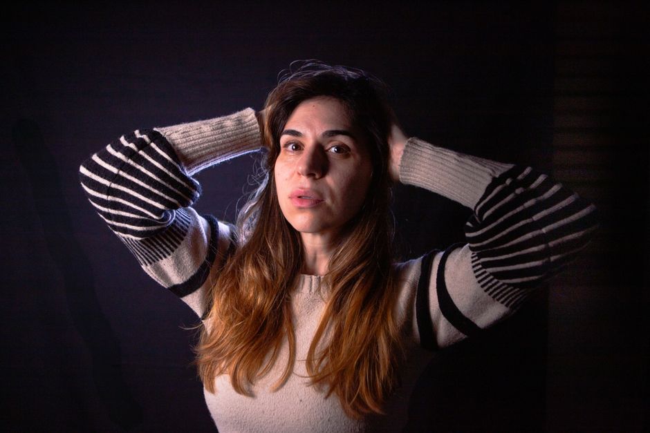 A woman poses confidently with hands in hair wearing a striped sweater, in a contemplative mood.