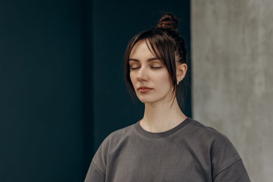 Serene young woman with closed eyes meditating indoors. Embracing tranquility and mindfulness.