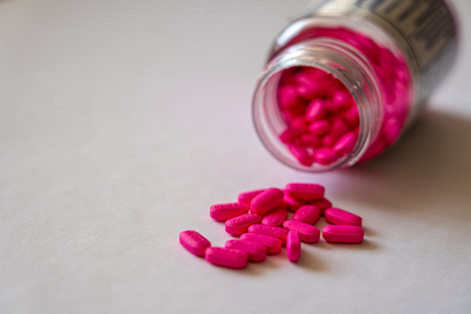 Close-up of an open bottle spilling pink pills onto a surface, indicating medication use.