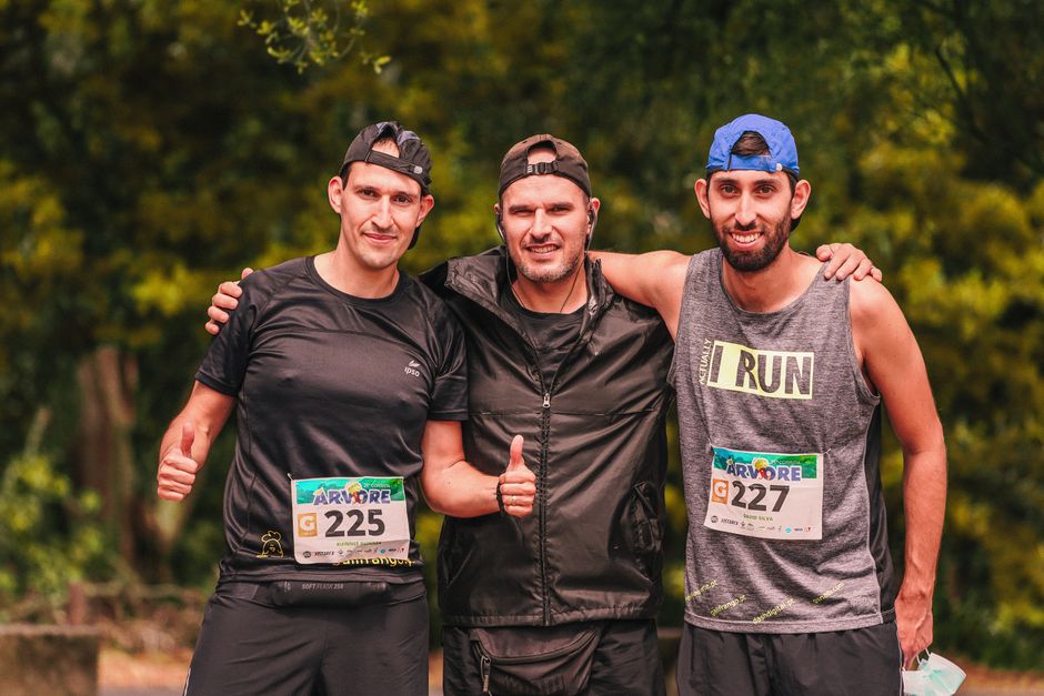 Three men, smiling, in sportswear giving thumbs up at an outdoor marathon event.