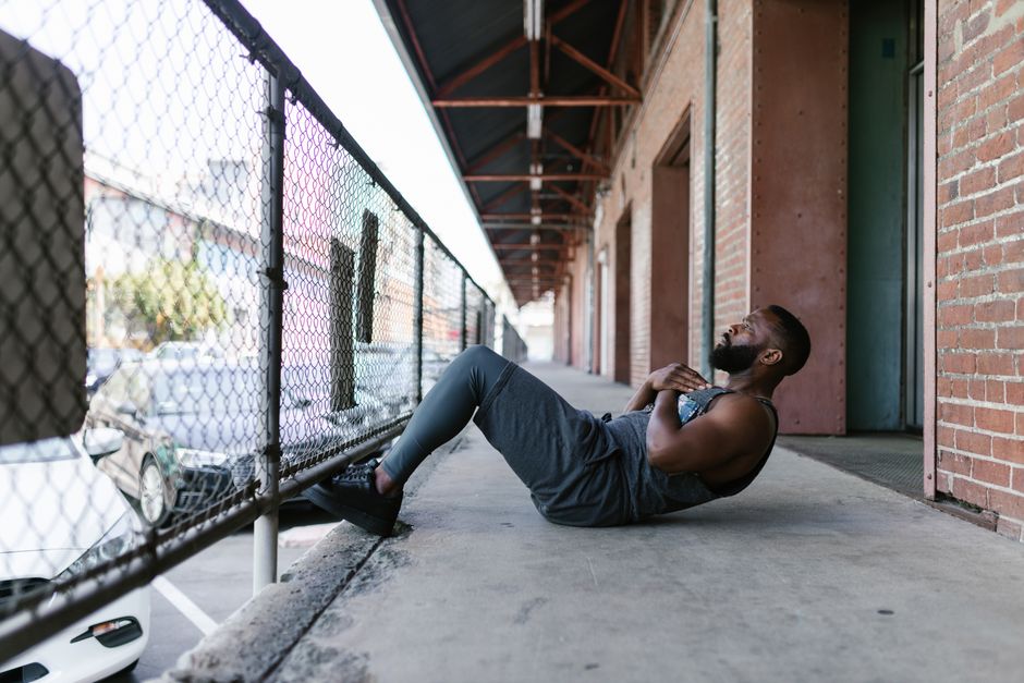 A man exercises outdoors doing sit-ups along a city walkway, enhancing fitness with street workout.