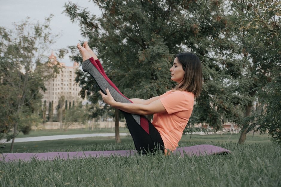 Woman practicing yoga outdoors, balancing in a yoga pose on a mat in a lush green park.