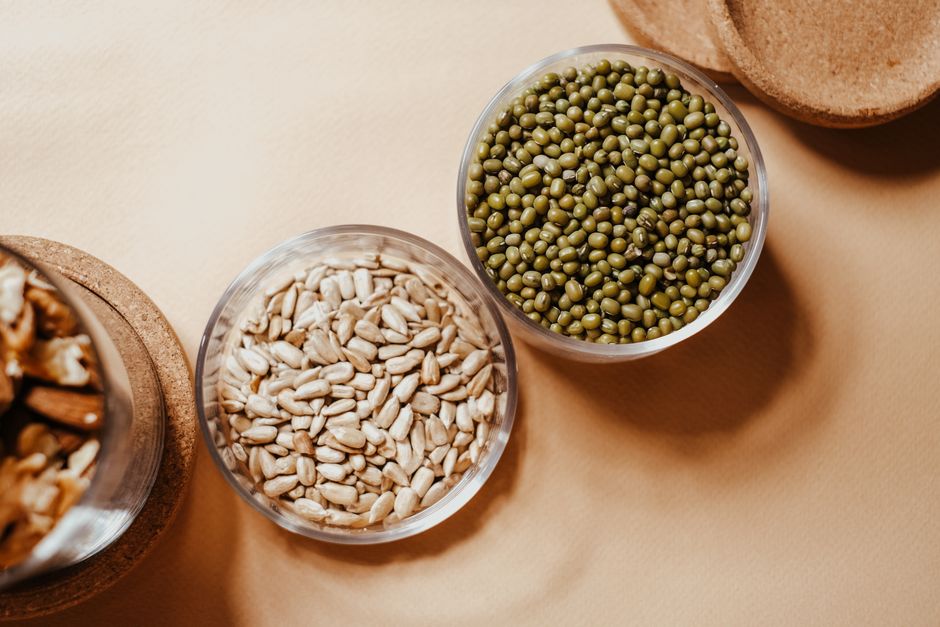 Glass bowls filled with organic mung beans and sunflower seeds on a neutral background.