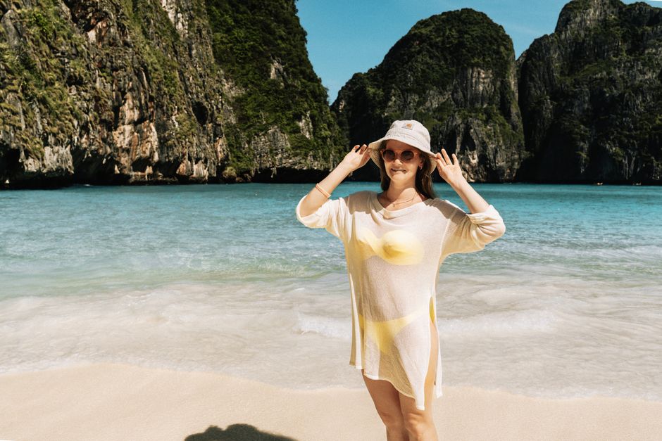 A woman in sun hat and dress enjoying the sunny beach at Maya Bay, Thailand.