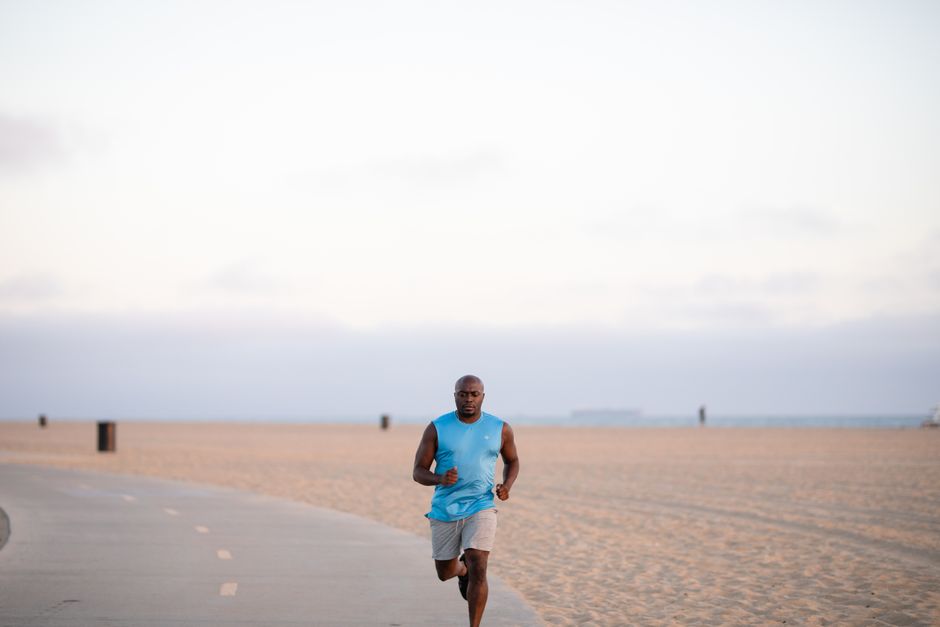 African American man jogging on a beach pathway, promoting fitness and healthy lifestyle.