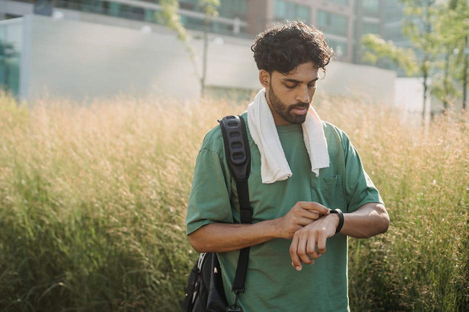 A young man with a towel checks his smartwatch while standing in an urban park.