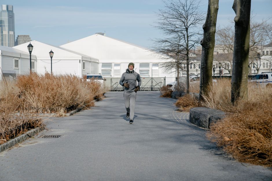 Full length of mature African American male wearing warm outfit jogging on asphalt roadway in park while training