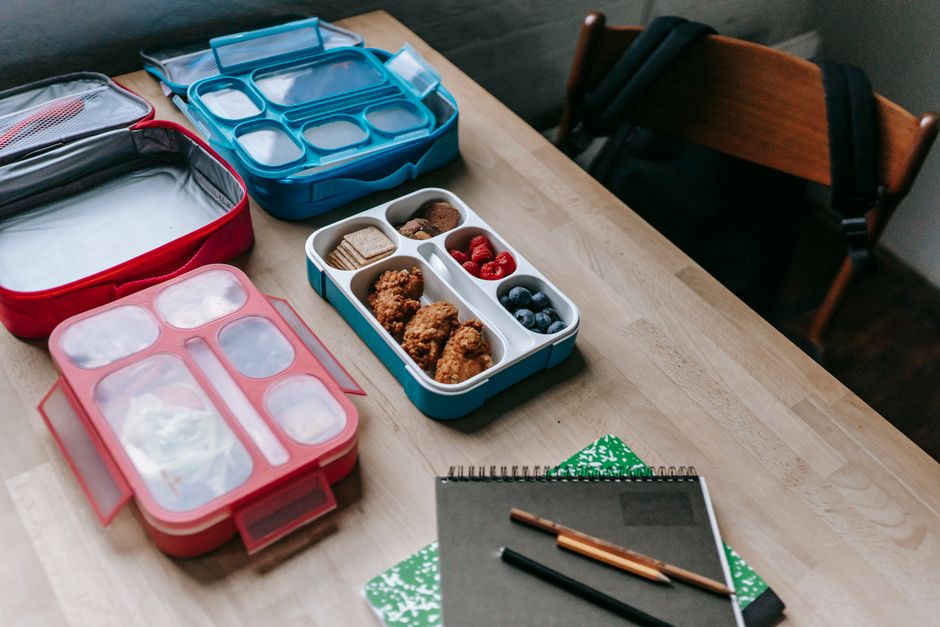 From above of lunch containers with fried chicken and fresh berries near crunchy cookies on table with copybooks