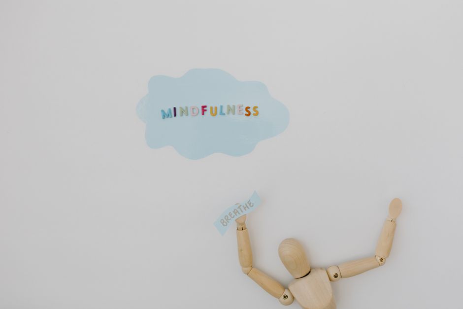 Wooden figure holding 'breathe' text with 'mindfulness' cloud on white background.
