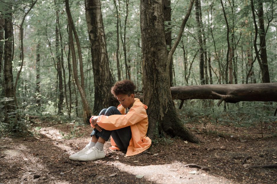 A young boy in a bright jacket sits alone in a serene forest, evoking emotions of solitude and reflection.