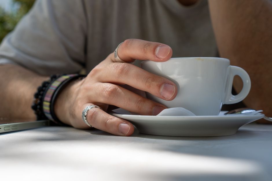 Close-up of a hand with rings holding a coffee cup outdoors, showcasing a relaxed lifestyle.