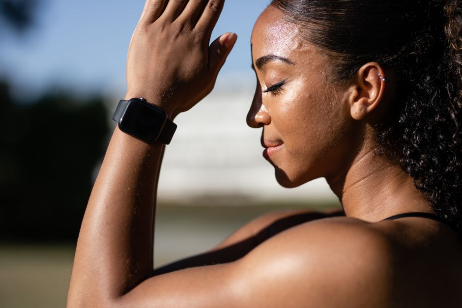 Side view of a calm African American woman meditating with a smartwatch outdoors.