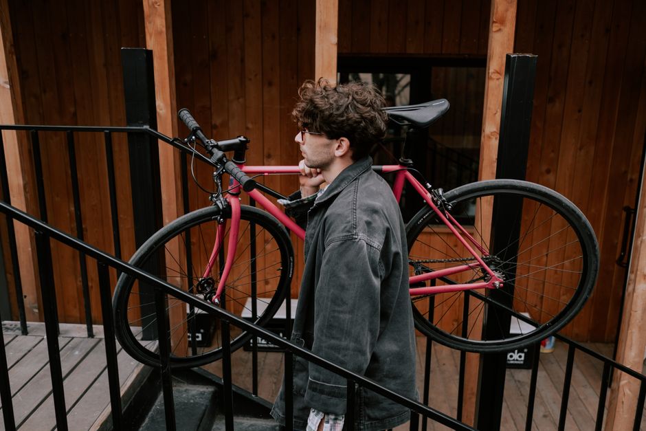 A man carrying a bike up wooden stairs, showcasing urban lifestyle and independence.