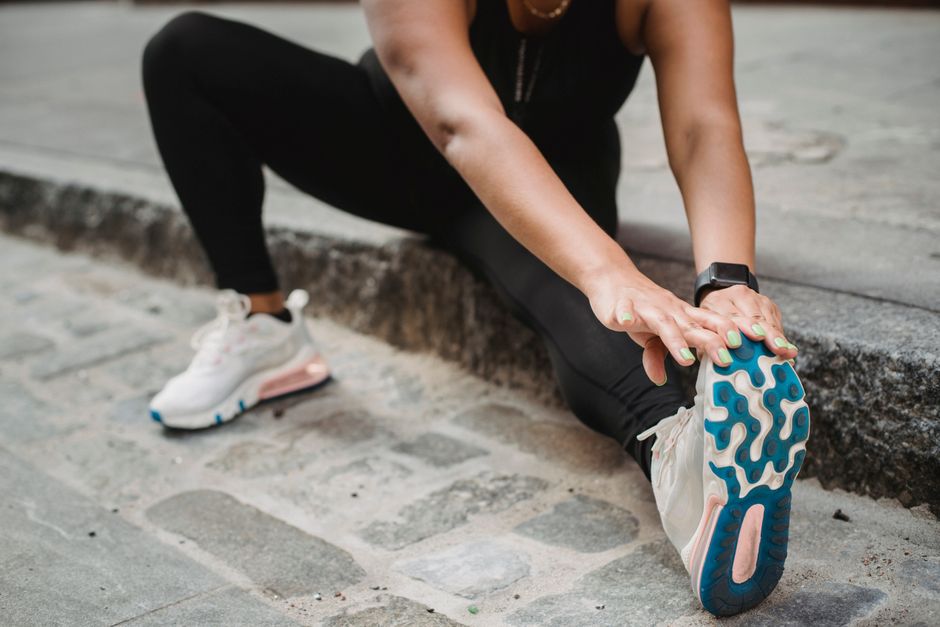 A woman in athletic apparel stretching on an urban sidewalk for fitness and flexibility.