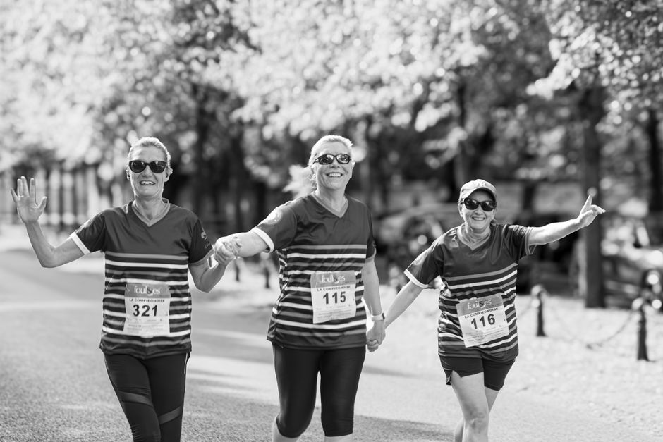 Three women enjoying a race together, holding hands and smiling outdoors.