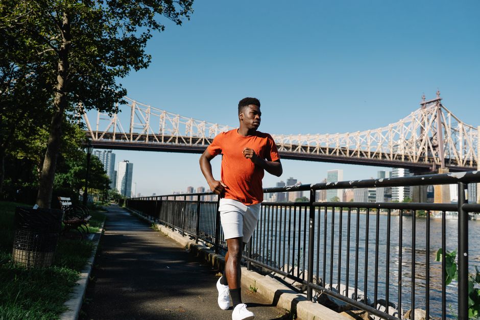 A man jogs alongside a river with a bridge in the background, enjoying a sunny day outdoors.