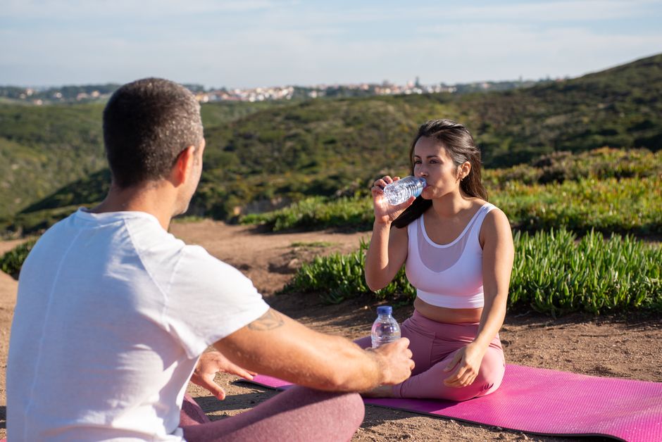 A man and woman enjoy an outdoor yoga session with water bottles in the scenic hills of Portugal.