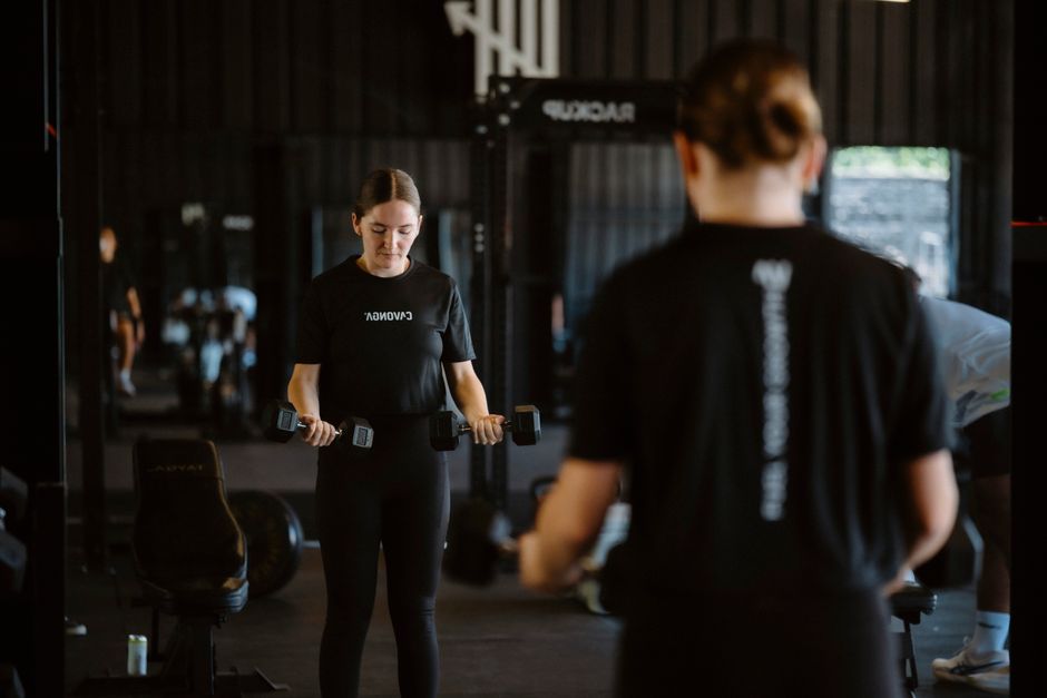 A woman performing a focused dumbbell workout in a modern gym setting.