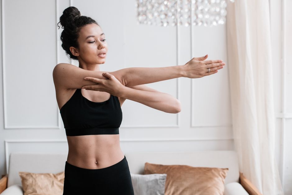 A young woman in activewear stretches indoors, embodying a healthy lifestyle.