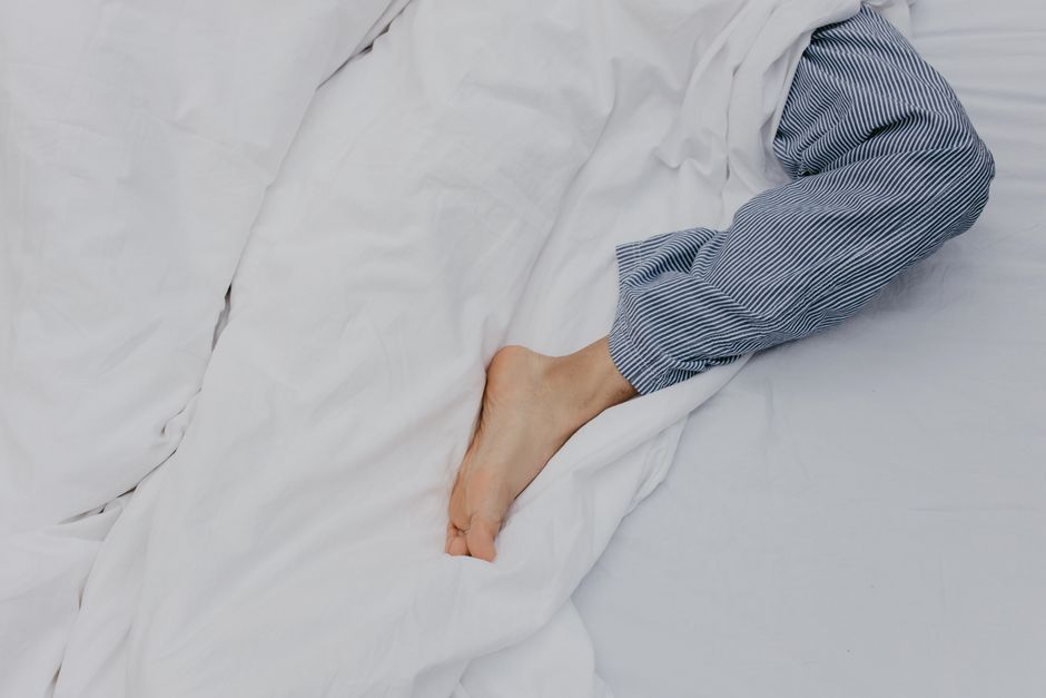 Relaxed morning with a foot peeking from under white bedding, wearing striped pajamas.