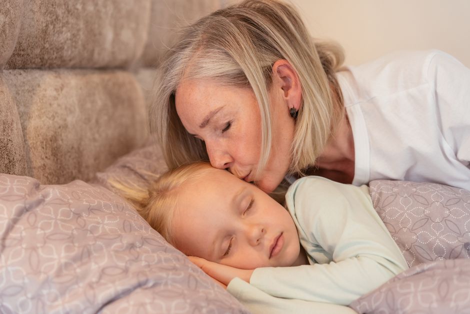 A loving grandmother kisses her sleeping grandchild in a cozy bedroom setting.