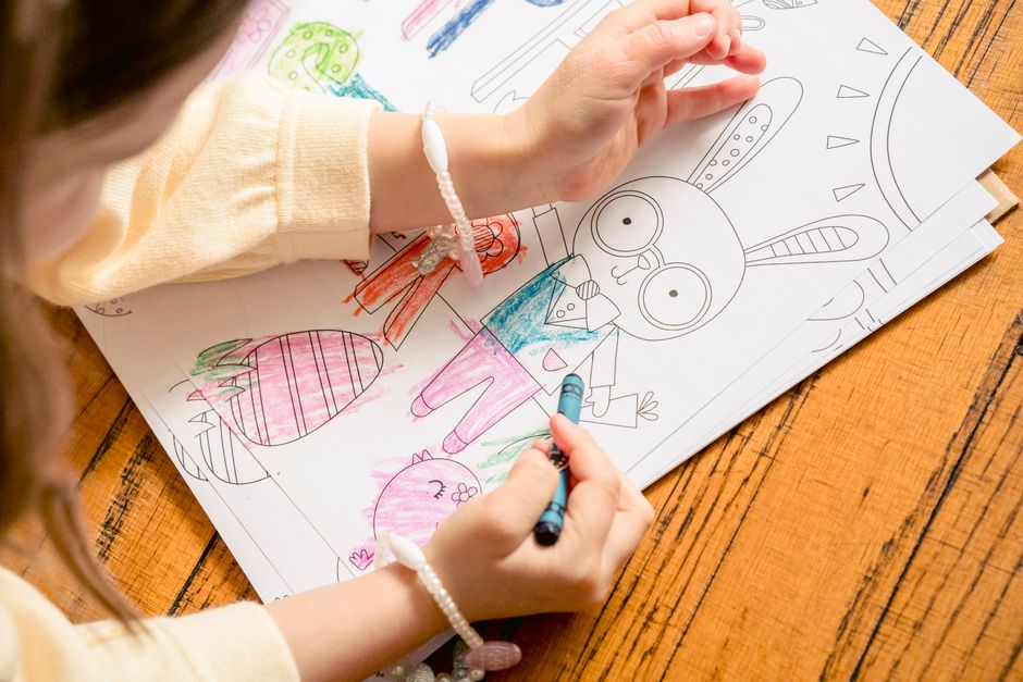 From above of crop unrecognizable girl in casual clothes drawing in coloring book in daylight