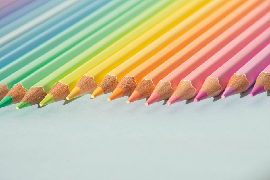 A close-up of colorful pencils arranged neatly, showcasing a rainbow gradient on a light background.