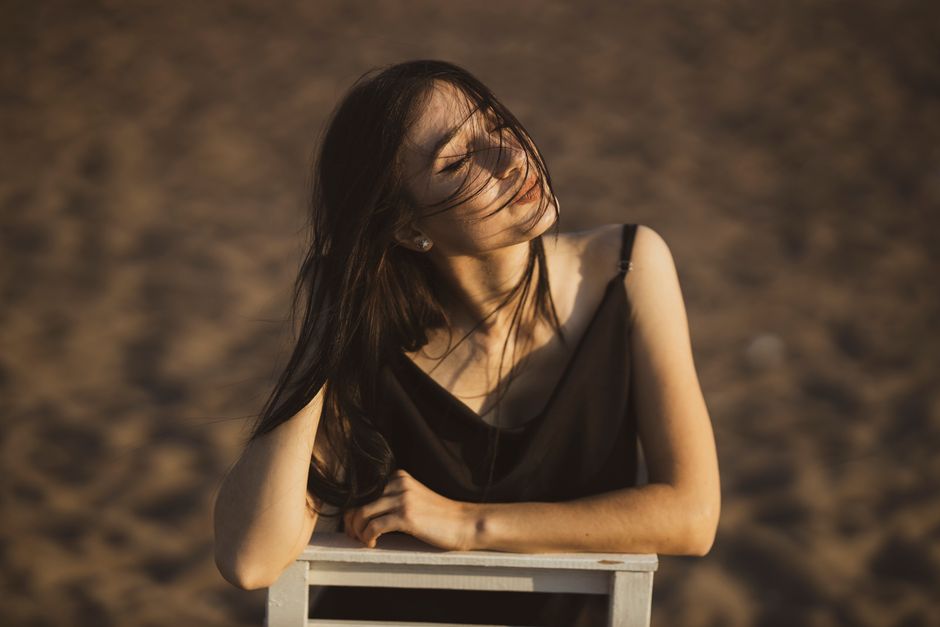 A woman with dark hair enjoying the warmth of the sun on a sandy beach.