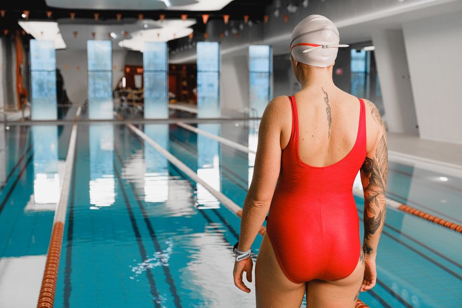 A woman with tattoos stands at an indoor pool, ready to swim.