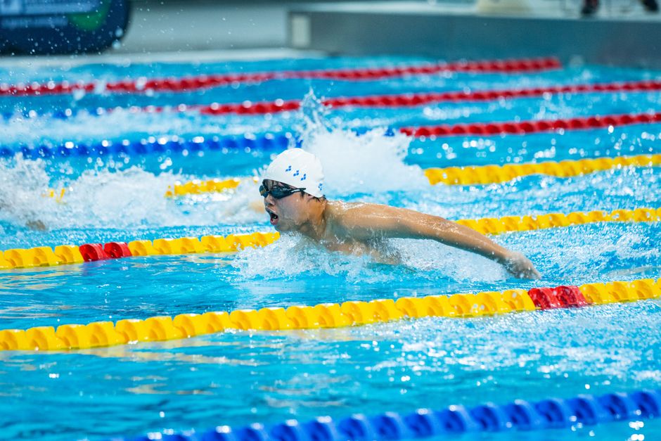 A focused swimmer competes in a swimming race at an indoor pool, showcasing athleticism and determination.