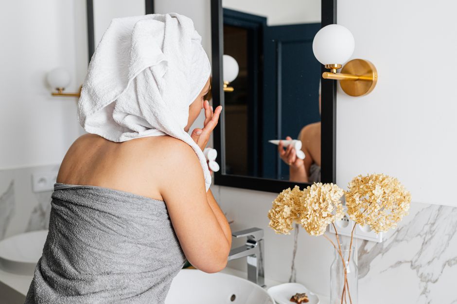 Woman in towel applies skincare in elegant bathroom with modern design, adding to her beauty routine.