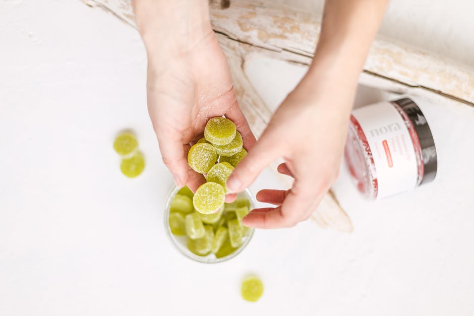 Close-up of hands holding green CBD gummies above a container, top view.