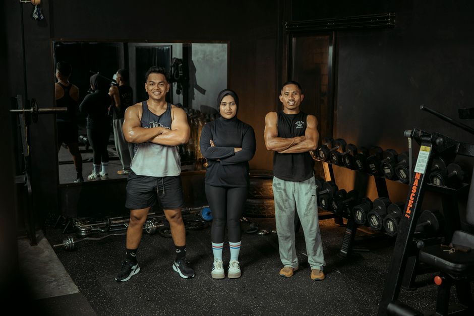 Three diverse individuals pose confidently in a gym, showcasing fitness and motivation.
