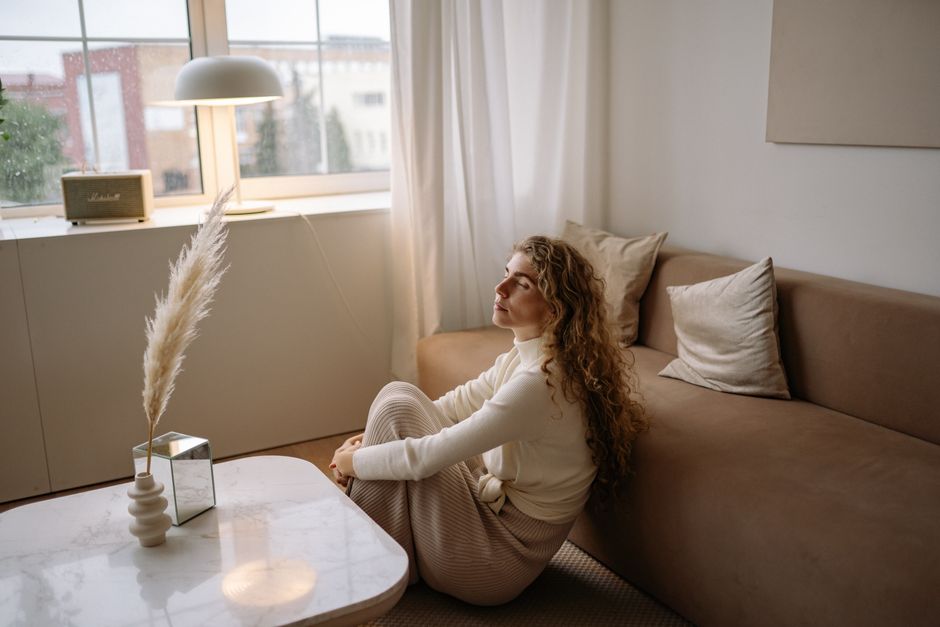 A woman sitting on a sofa in a calm, minimalist living room setting.