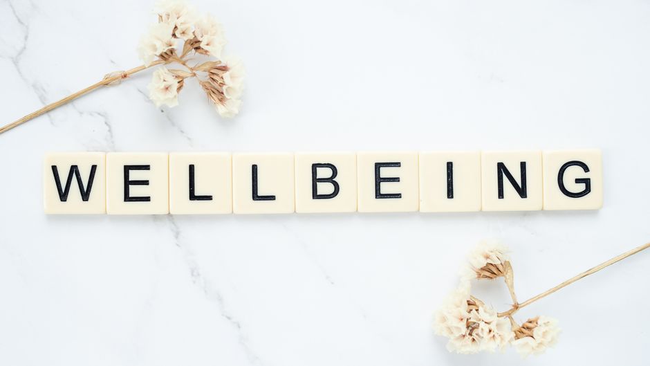 Scrabble tiles spell 'Wellbeing' amid delicate white flowers on a marble background.